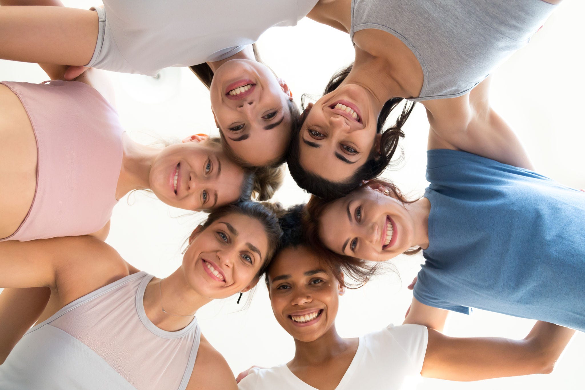 Low angle of smiling toned girls stand in circle hugging looking at camera, excited female yogi embrace, feel motivated at yoga session, happy women involved in teambuilding show unity and support